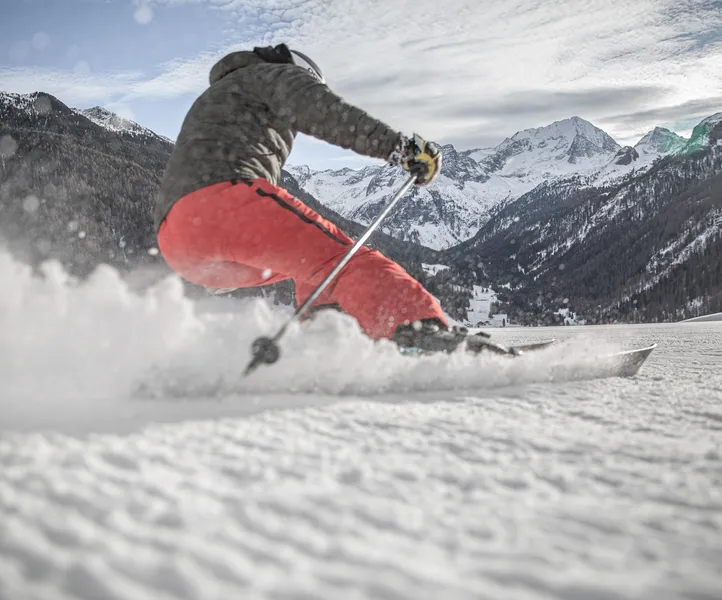 Skifahrer beim dynamischen Carving-Schwung mit aufstiebendem Schnee auf einer Piste im Ahrntal