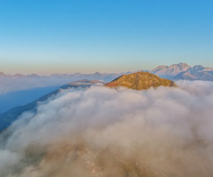 Berggipfel im Ahrntal über dem Wolkenmeer mit Blick auf die Zillertaler Alpen bei Sonnenaufgang