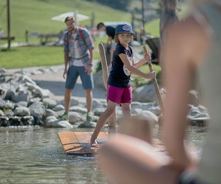 Kind auf Holzfloß am Naturerlebnis-Wasserspielplatz am Klausberg, Ahrntal Südtirol