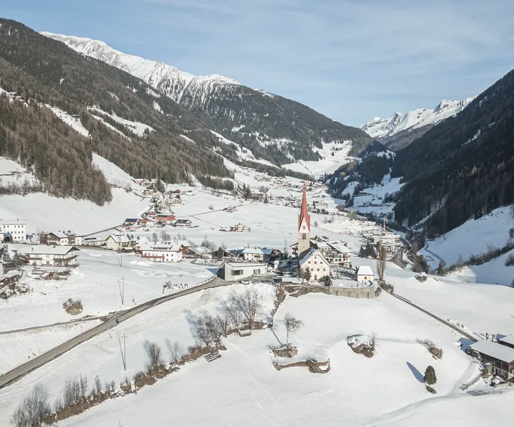 Verschneites Dorf im Ahrntal mit markanter Kirche, umgeben von Südtiroler Bergen im Winter