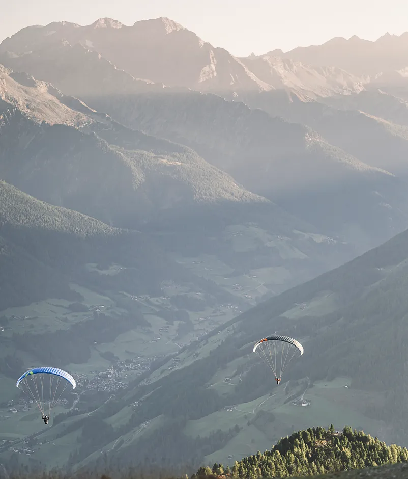 Due parapendii con vele colorate nel sole serale sopra la verde Valle Aurina, Alto Adige