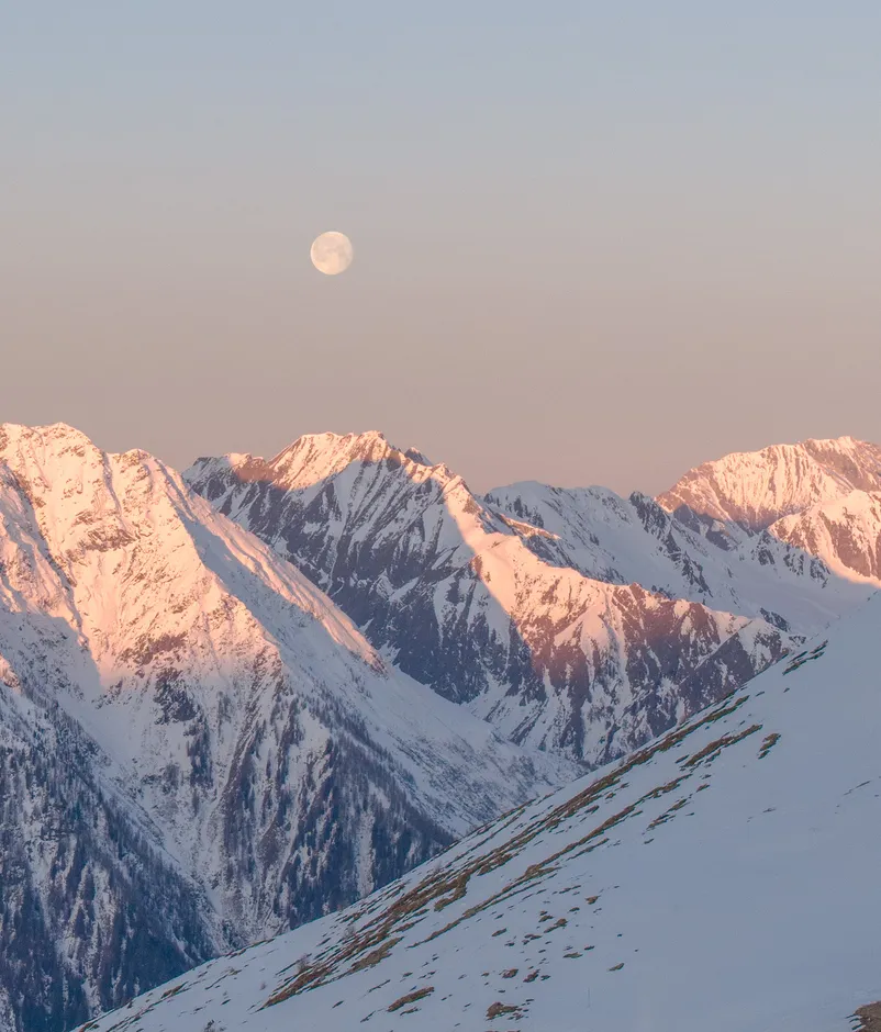 Vollmond über den alpenglühenden Gipfeln der Zillertaler Alpen in der Abenddämmerung über dem Ahrntal