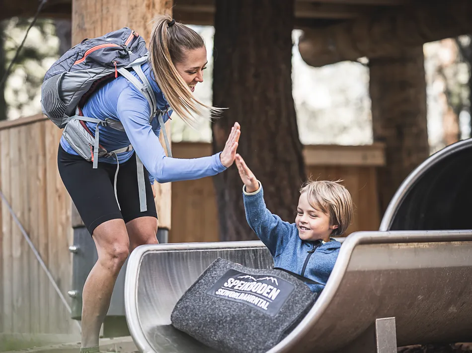 Mutter gibt Sohn High-Five an der Speikboden-Rutsche im Bergwald, Sommer-Familienattraktion
