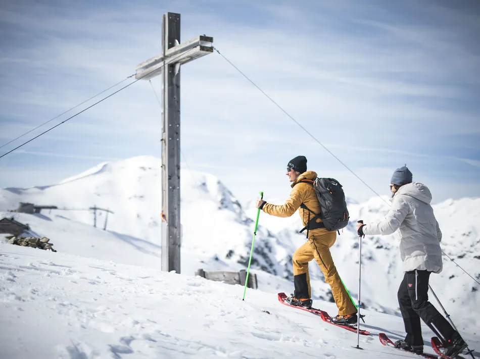 Escursionisti con ciaspolette in salita verso la croce di vetta allo Speikboden con panorama alpino invernale