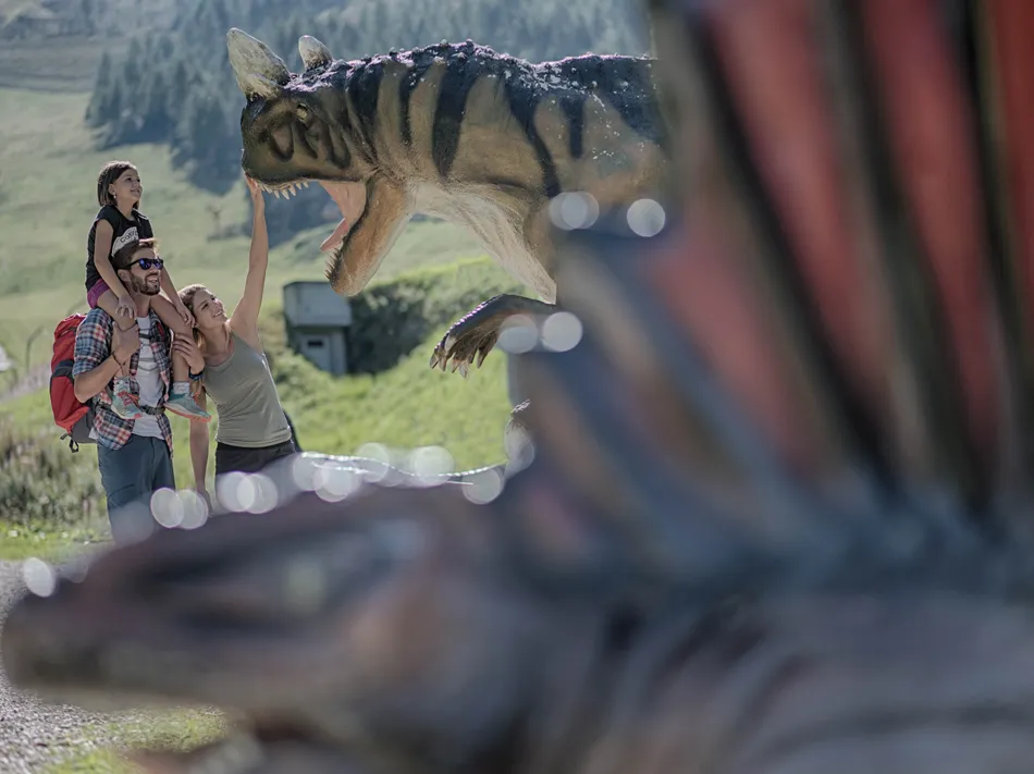Familie mit Kind entdeckt lebensgroße Dinosaurier-Figur im Dinopark am Klausberg im Ahrntal