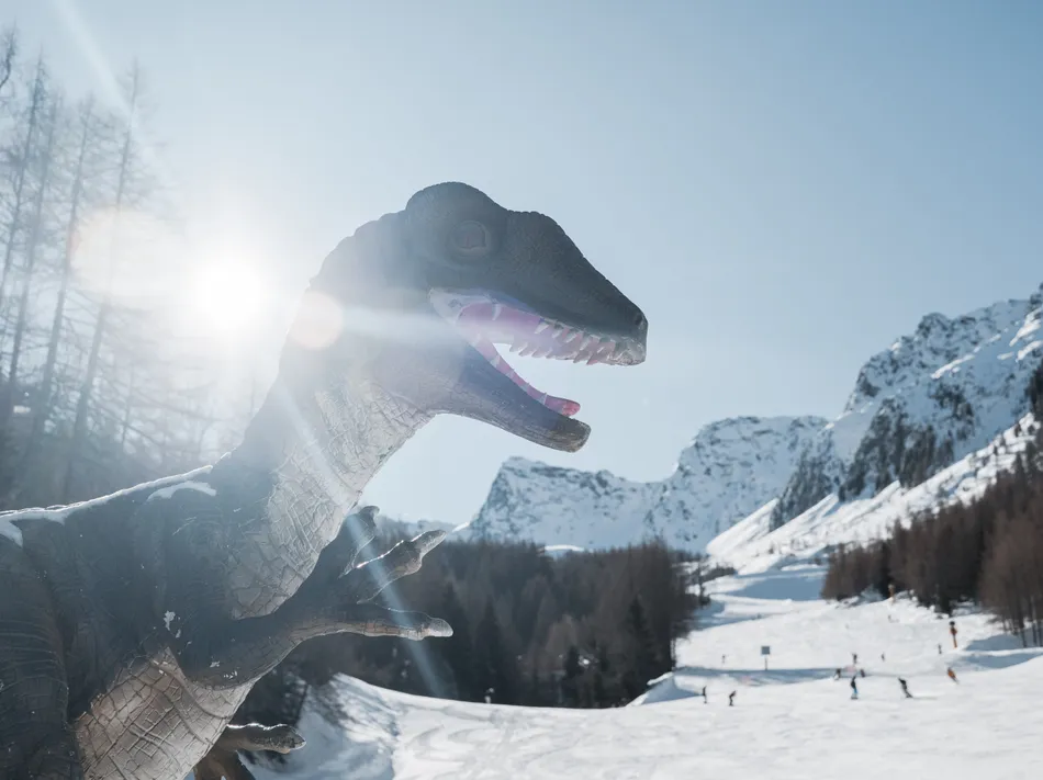 Figura di dinosauro nel Dino-Park al Klausberg con pista da sci e montagne innevate sullo sfondo