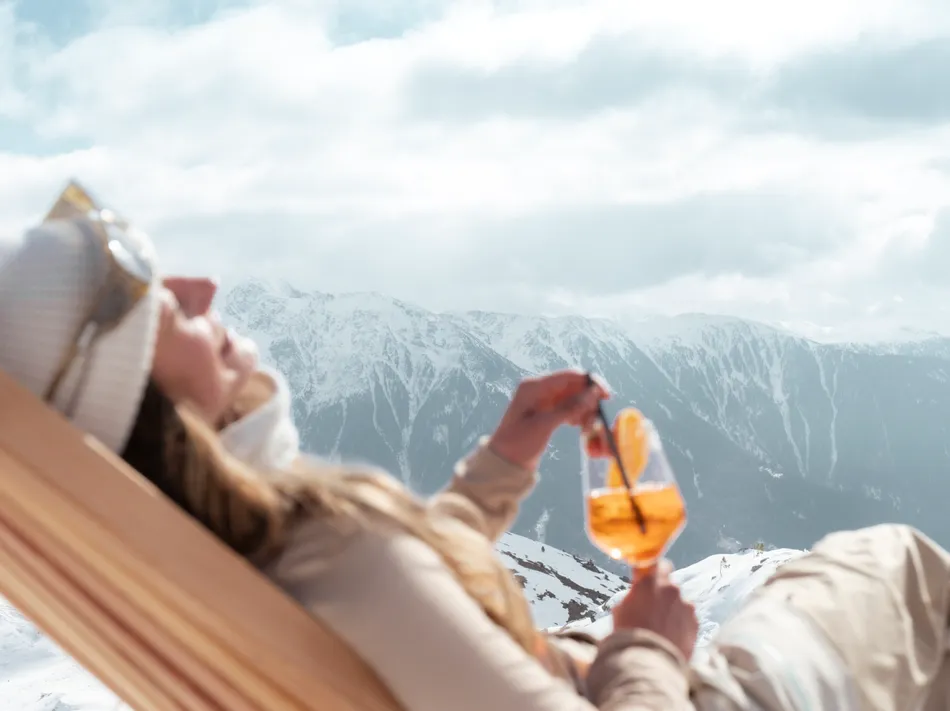 Après-ski atmosphere at Klausberg: woman with Aperol Spritz on a deckchair facing the mountains