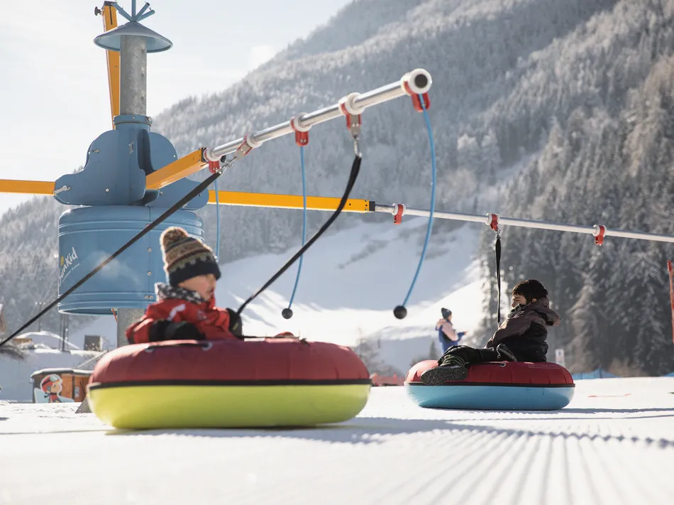 Children on colorful snow tubes on the tubing carousel in the kids' area in Ahrntal
