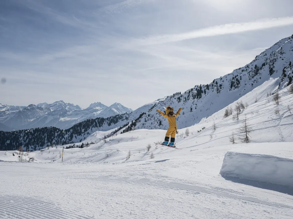 La mascotte dello skigebiet in costume giallo salta sugli sci su un kicker in Valle Aurina