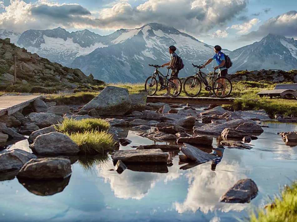 Two e-mountain bikers in front of the glacier panorama of the Zillertal Alps on a tour in Ahrntal